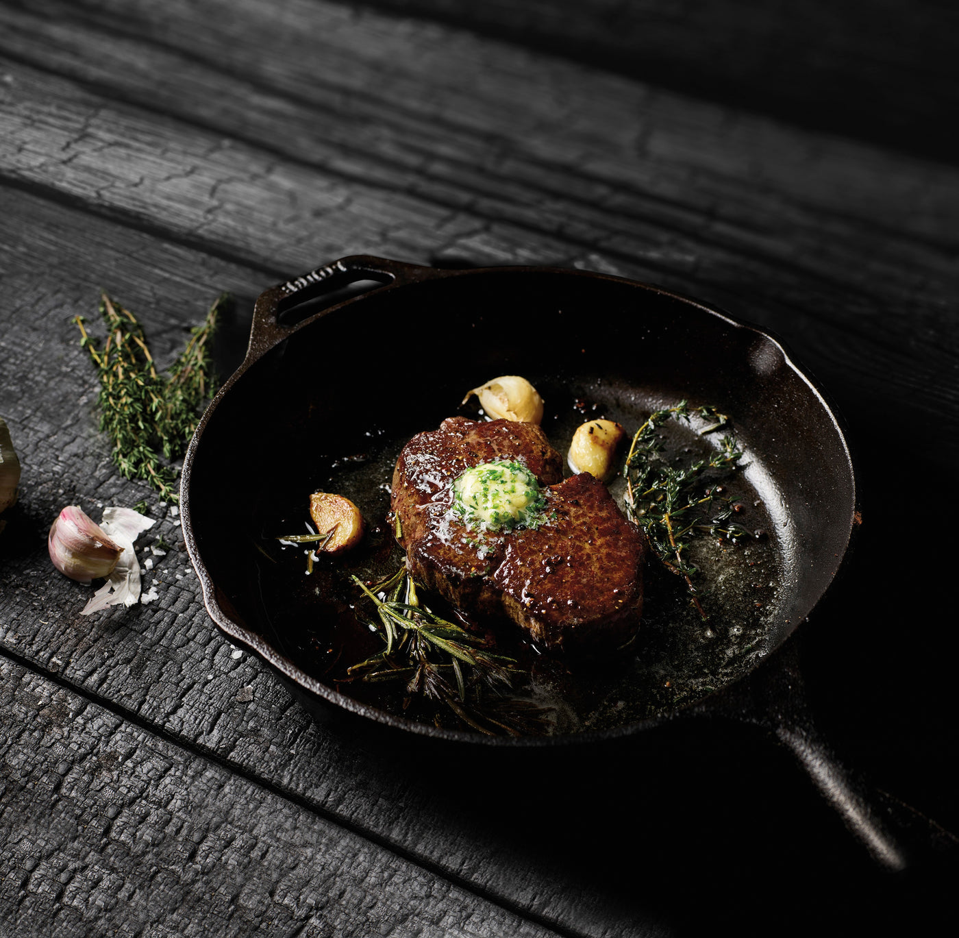 Grilled Filet Mignon steak with garlic and herbs in a cast iron skillet on a wooden surface
